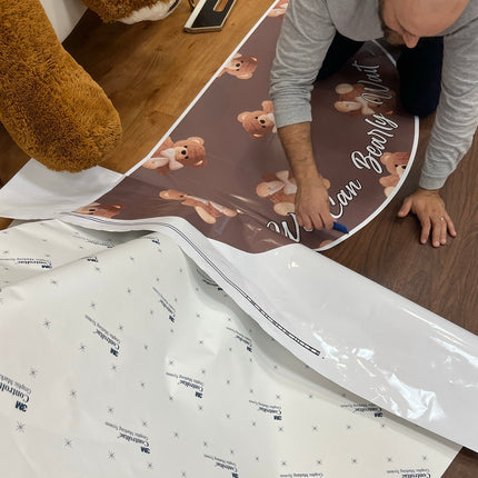 Custom die cut floor adhesive being applied on a wooden floor featuring a bear design.