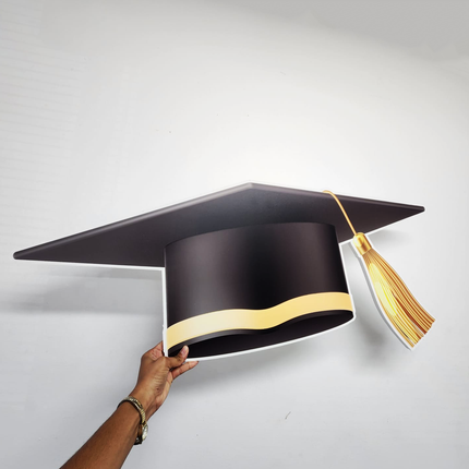 Hand holding custom graduation cap cutout with black cap and gold tassel against white background