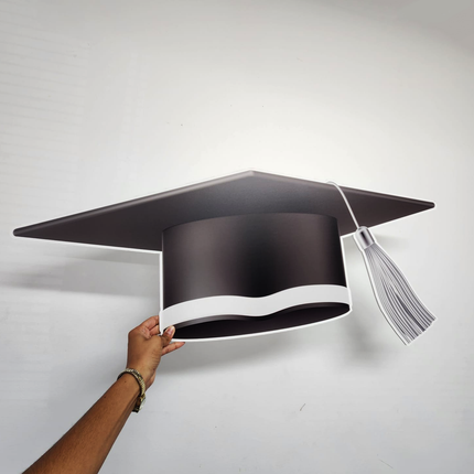 Hand holding a black and white custom graduation cap cutout with tassel on a white background