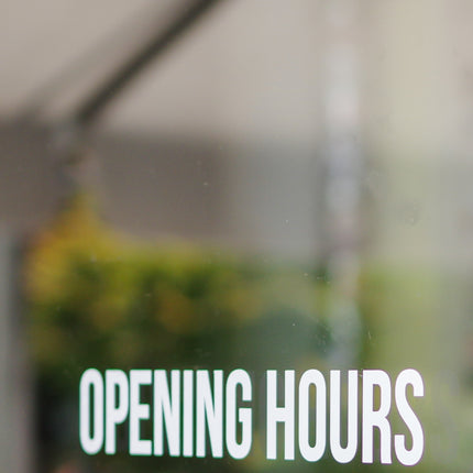 WPEProduction white custom window decals displaying opening hours on glass door