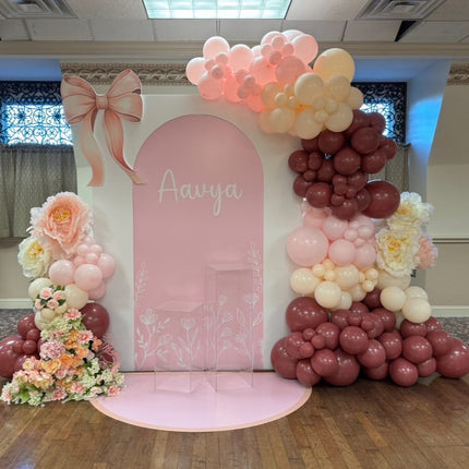 Double arch floral set with Bow backdrop featuring pink and maroon balloons and large floral decorations