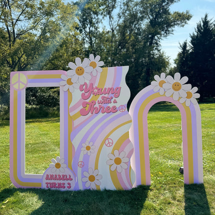 Colorful groovy birthday backdrop decorations with daisies and peace signs for a third birthday party