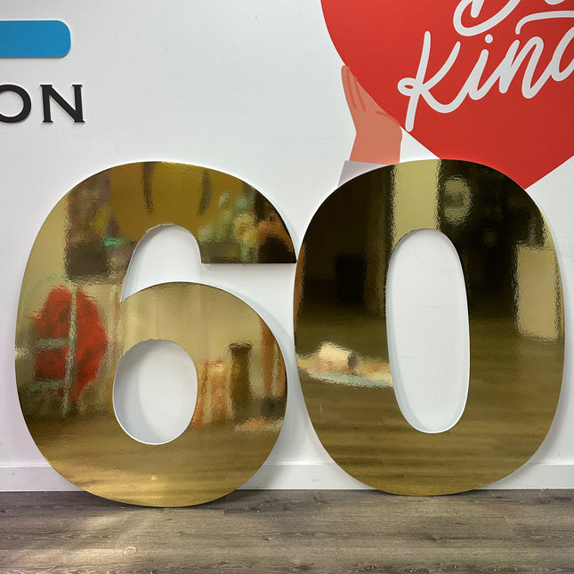 Large metallic number display in gold showing number 60 on wooden floor against white wall