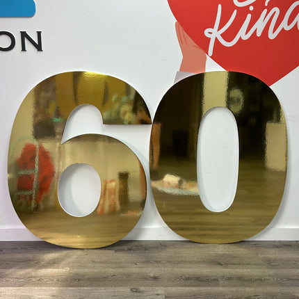 Large metallic number display of gold color showing the number 60 standing on wooden floor