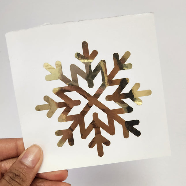 Hand holding a square white sheet with a metallic gold decals snowflake design