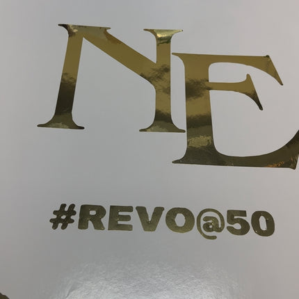 White surface with metallic gold decals showing letters NE and hashtag REVO at 50