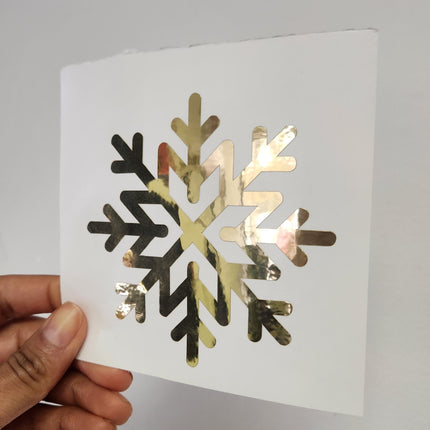Hand holding white square sheet featuring a metallic gold decals snowflake design