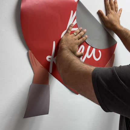 Person applying large red heart-shaped personalized vinyl sticker printing on a white wall