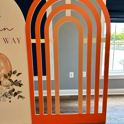 Orange rainbow foam board backdrop with arched cutouts standing indoors on wooden floor