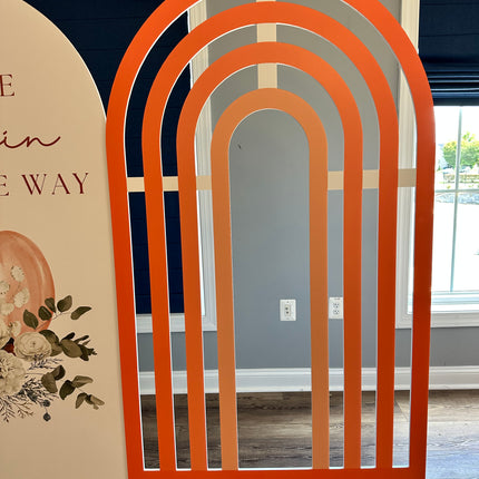 Orange rainbow foam board backdrop with arch design standing indoors on wooden floor